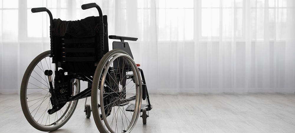 Wheelchair against window, in bright living room or hospital interior.